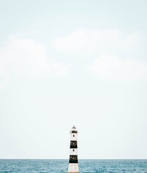 晴朗的天空与平静的海面之间，矗立着一座孤独的灯塔，展现出极简主义的宁静