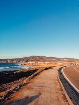 A picturesque coastal highway winds along the beach with mountains and ocean in view.