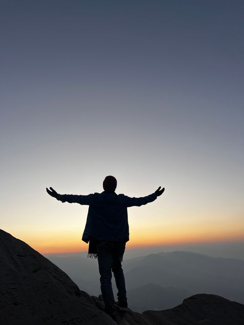 Free Silhouette of a person with open arms on a mountain at sunset, symbolizing freedom and adventure. Stock Photo