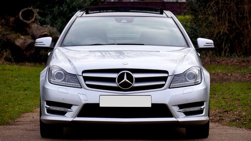 Free Front view of a sleek silver luxury coupe car parked on a road, surrounded by greenery. Stock Photo