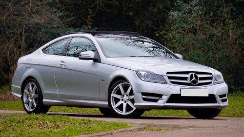 Free A sleek silver Mercedes-Benz coupe parked on a quiet, scenic road surrounded by greenery. Stock Photo