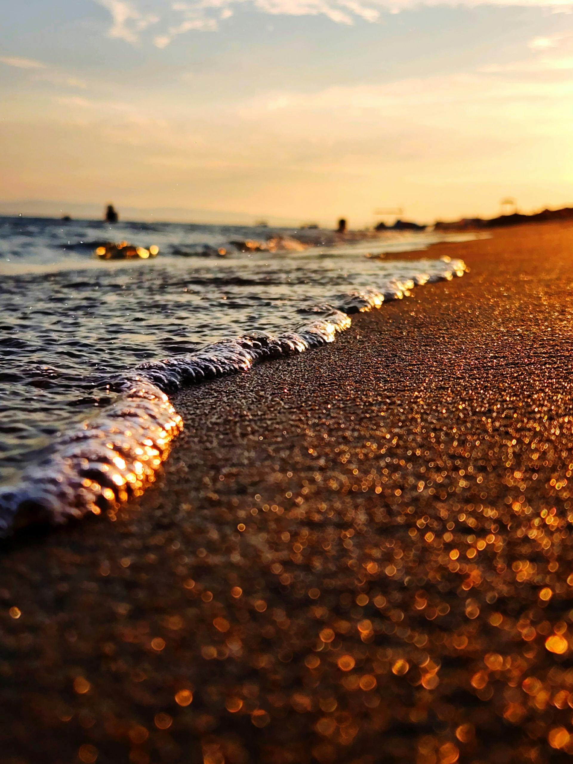 Close-up of gentle waves on sandy beach during a vibrant sunset with golden hues.