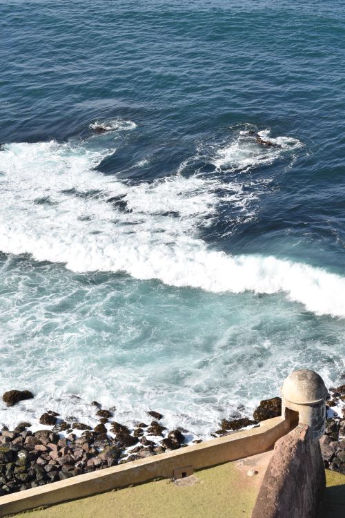 Free Aerial view of ocean waves hitting a rocky shoreline with an ancient fort wall in the foreground. Stock Photo