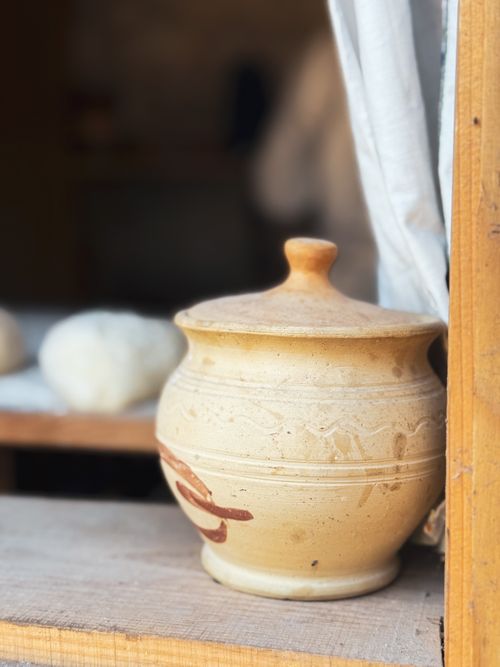Free A rustic clay pot with lid on a wooden shelf, capturing natural light and soft focus background. Stock Photo
