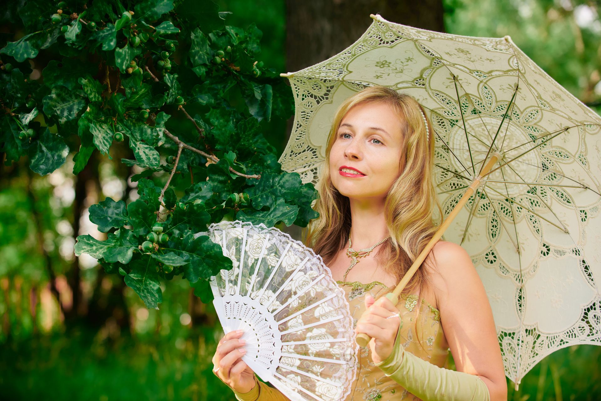 A graceful woman holding a lace parasol and fan in a verdant outdoor setting.