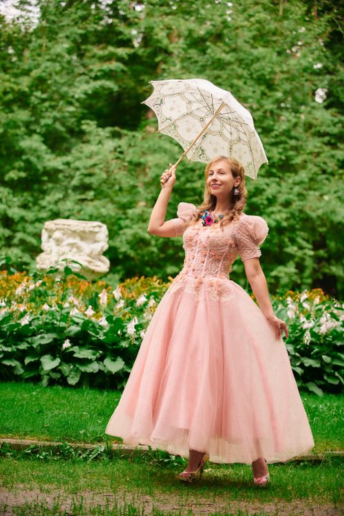 Free Woman in Victorian pink dress holding a decorative parasol in a lush garden setting. Stock Photo