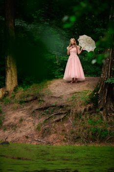 Adult female standing in a forest with a pink dress and umbrella, evoking a fairy tale ambiance.