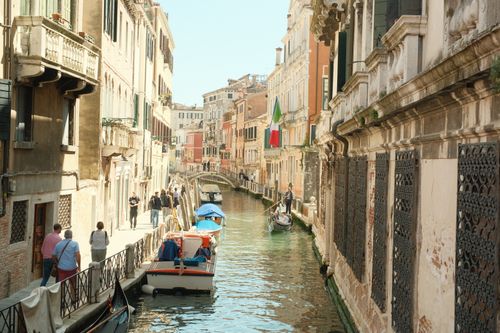 Free A picturesque view of a Venetian canal with a gondola, showcasing classic Italian architecture and vibrant life. Stock Photo