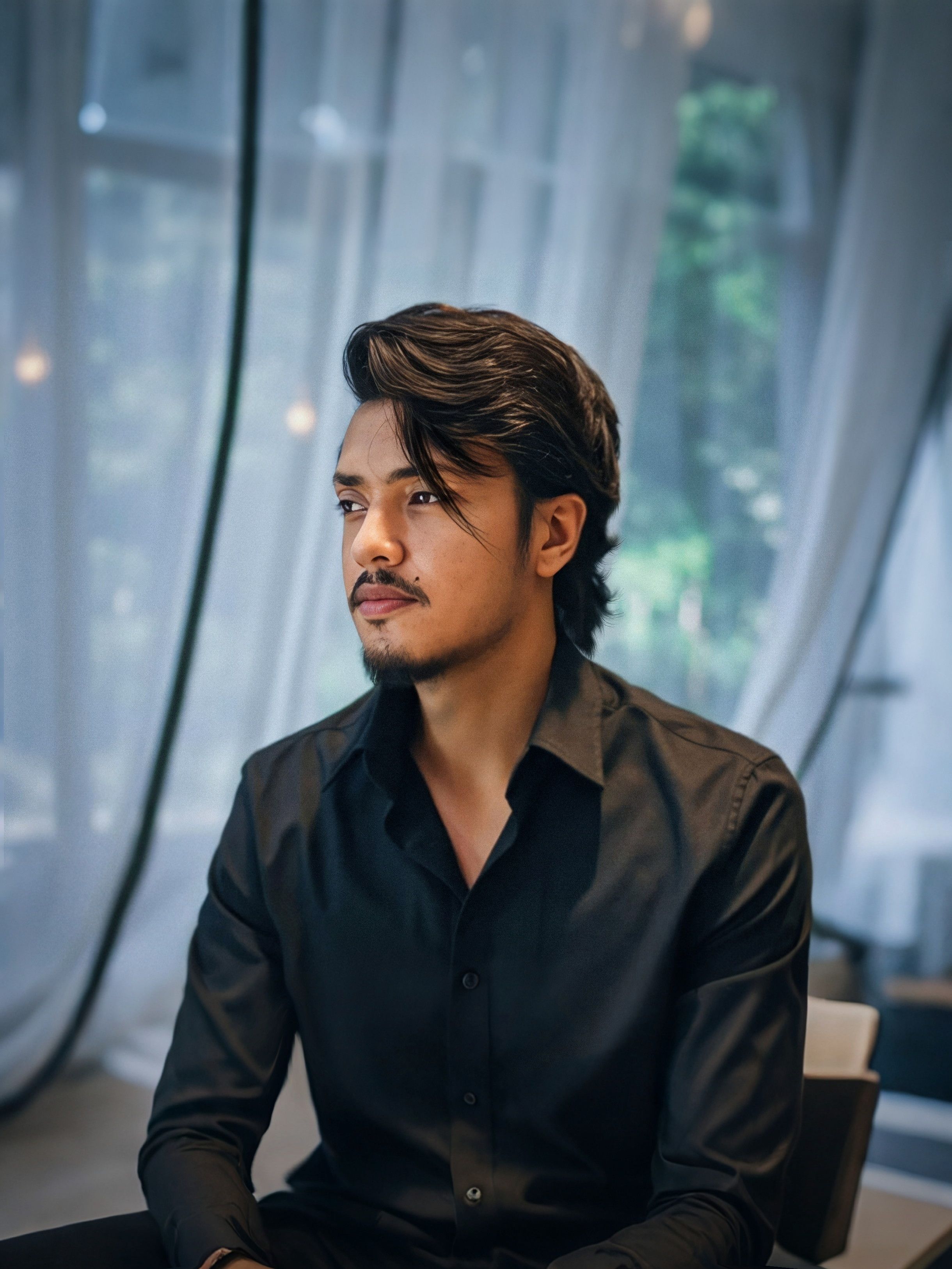 Portrait of a thoughtful man in a black shirt seated indoors with a serene backdrop.