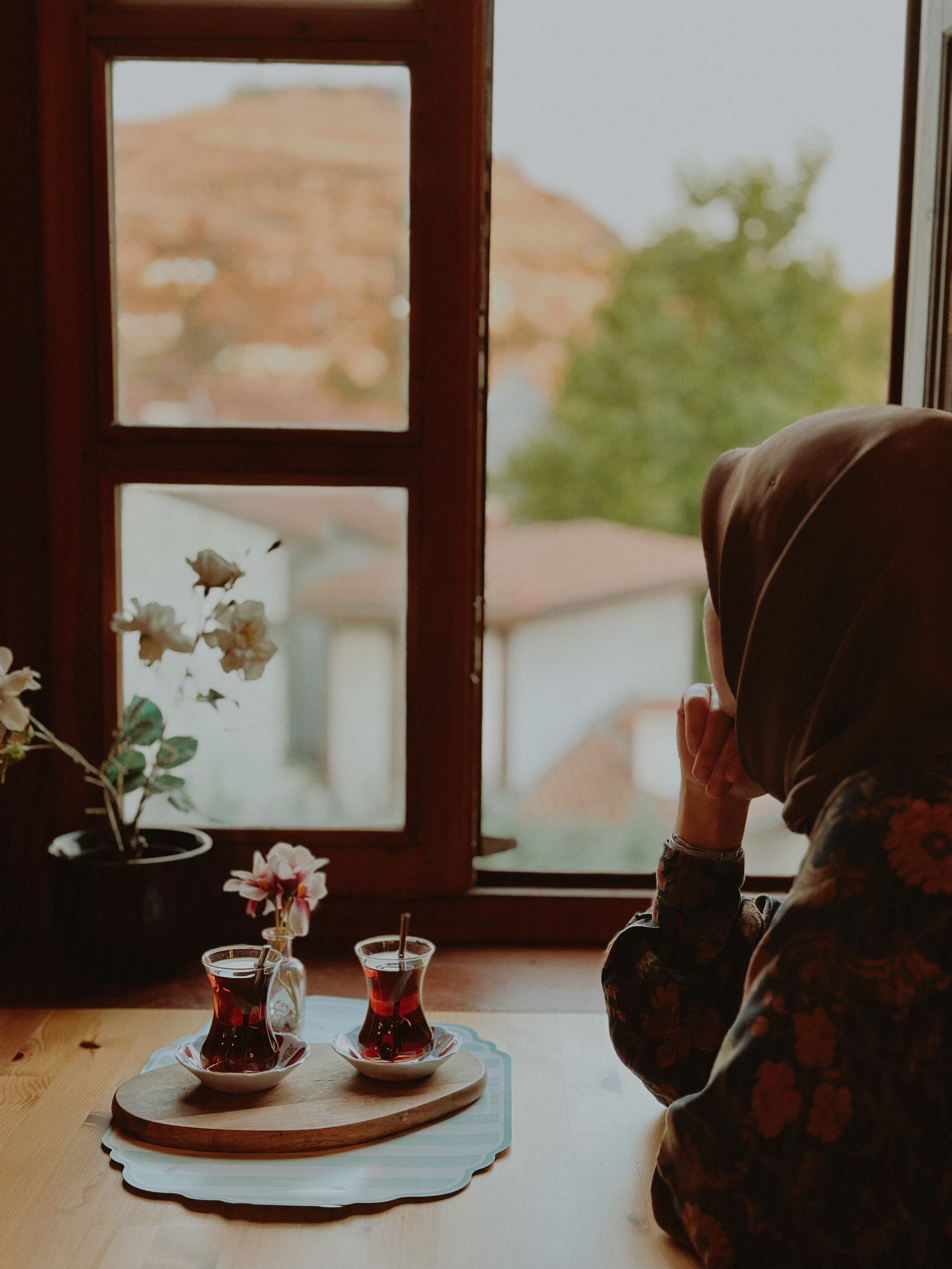 Woman enjoys black tea at wooden window with scenic view of Ankara. Warm, vintage vibe.