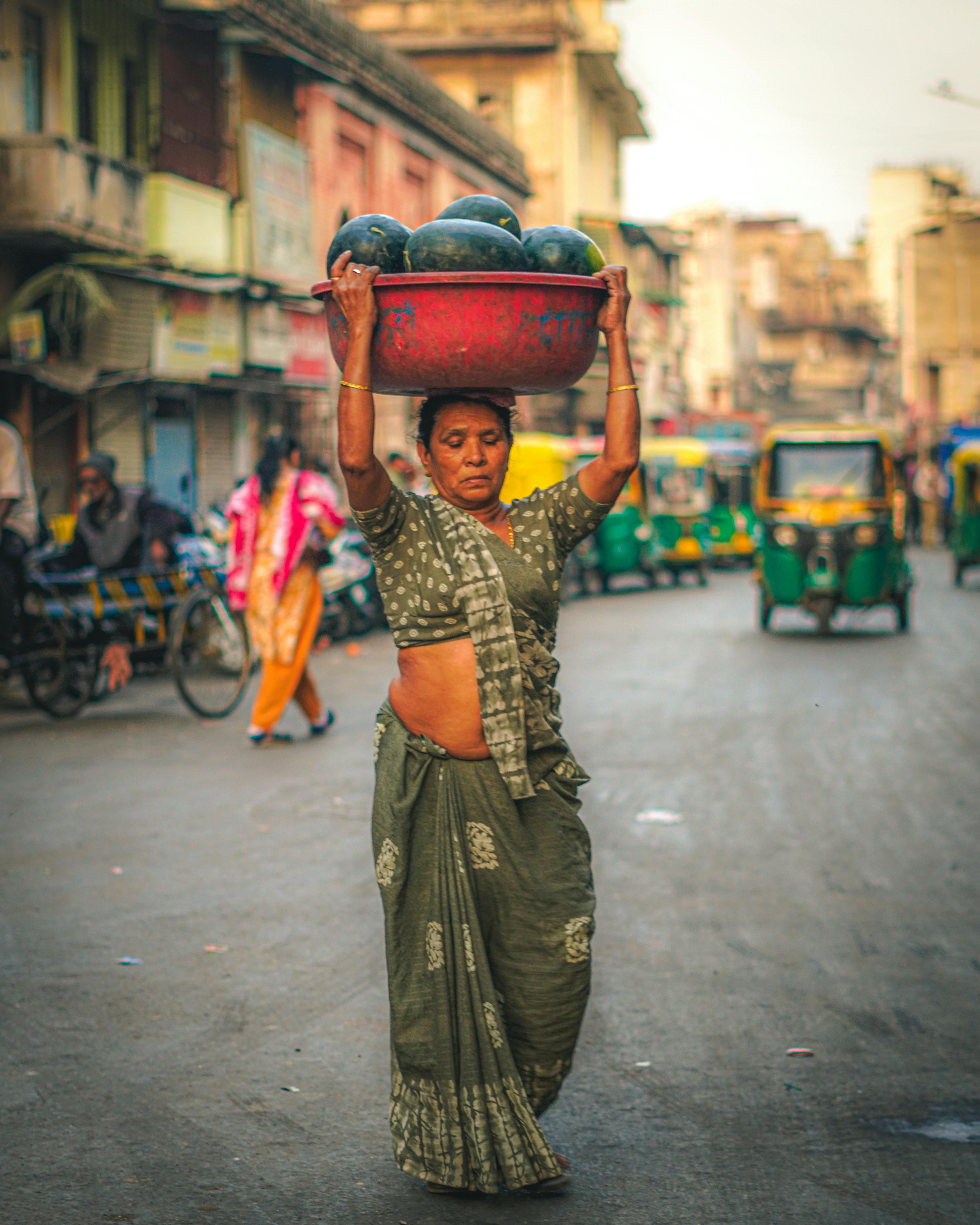 Woman in traditional attire carrying watermelons on street of Ahmedabad, India.