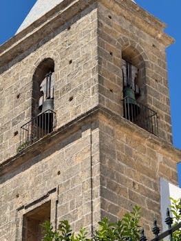 Close-up of a historic bell tower with stone facade under a clear blue sky in Cádiz, Andalucía.