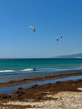 Two kitesurfers enjoying the sunny shores of Cádiz, Spain, showcasing vibrant ocean and blue skies.