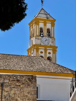 Charming clock tower with rustic architecture in Málaga, Spain, set against a vibrant blue sky.
