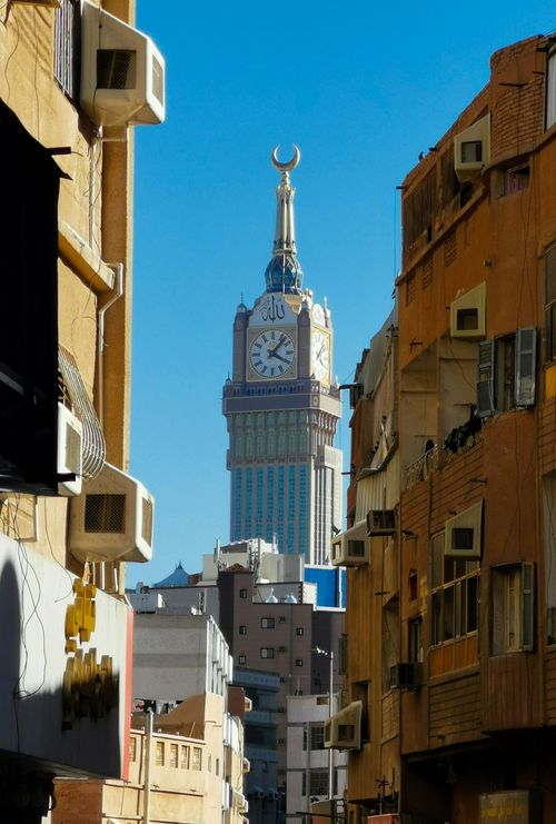 Free View through urban alley of Abraj Al Bait clock tower under clear blue sky. Stock Photo
