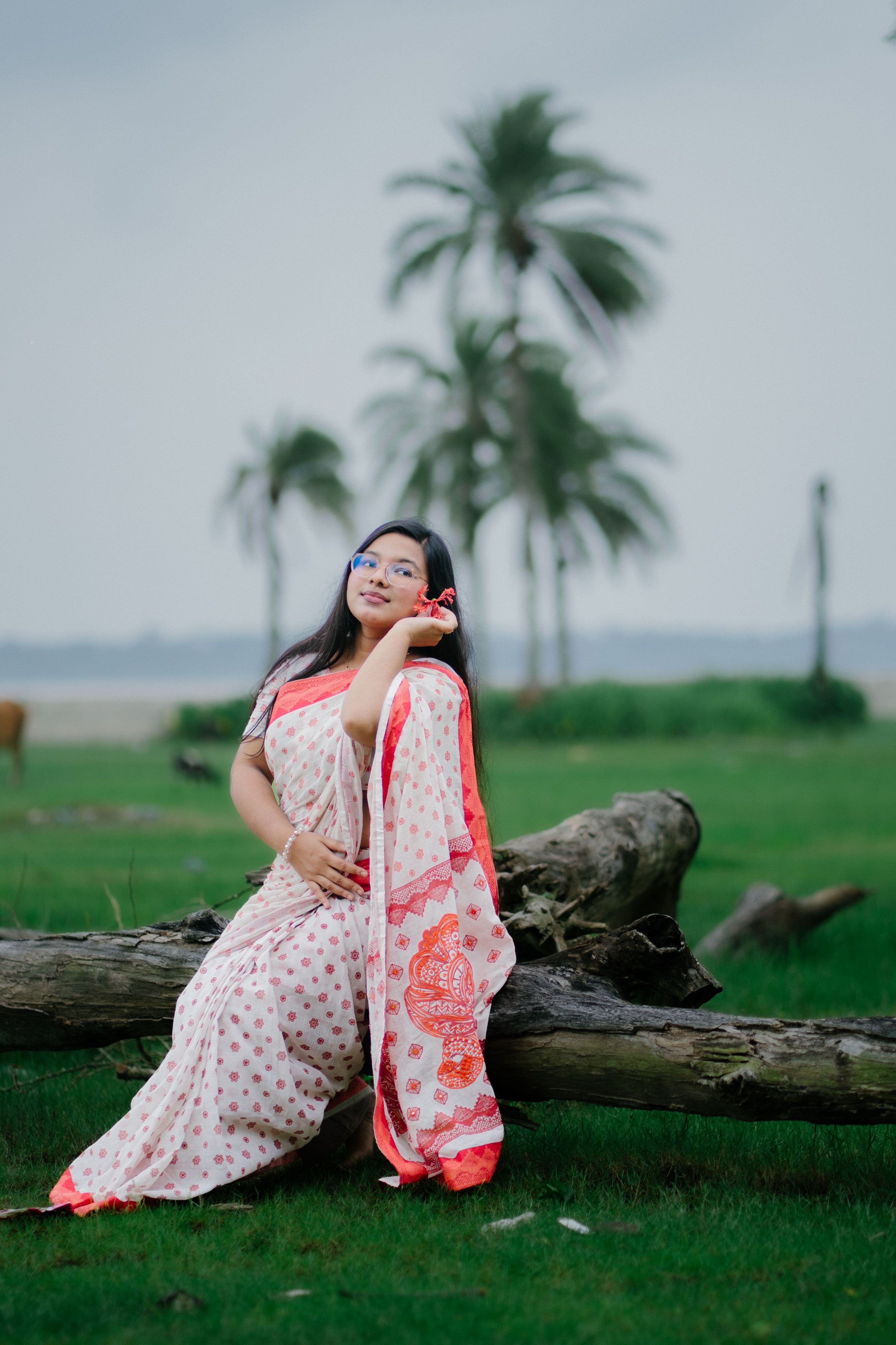 Woman in saree with serene expression in a lush landscape setting with palm trees.
