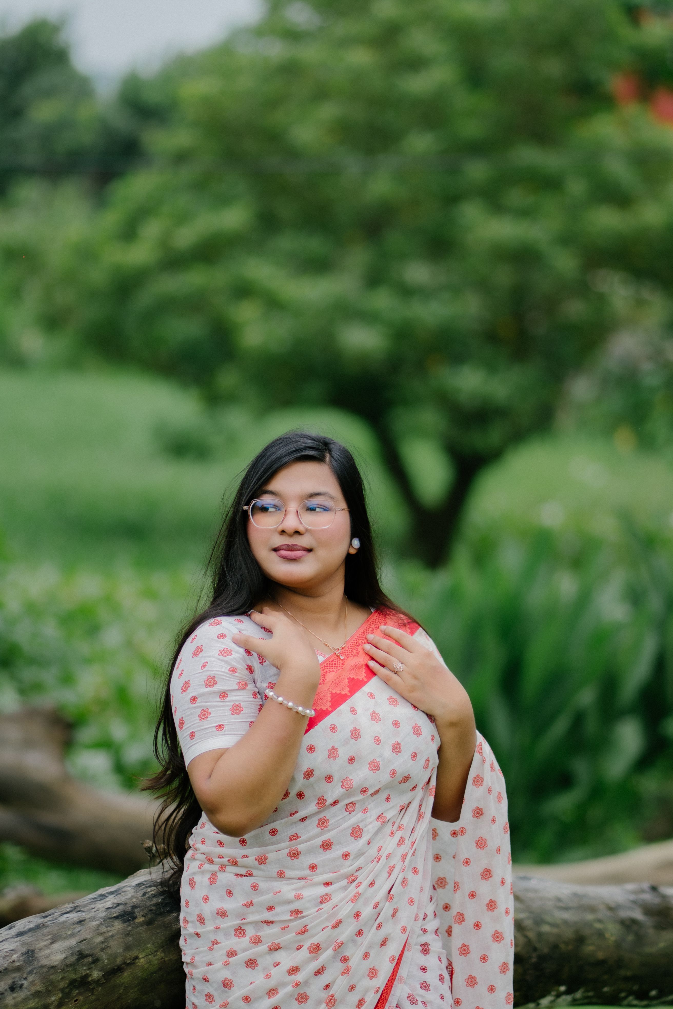 A young woman in a polka dot sari posing outdoors in a lush green setting.