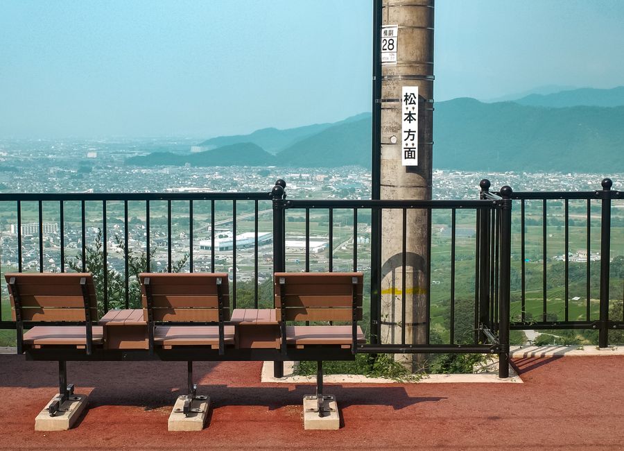 Tranquil hilltop view overlooking Nagano, Japan with empty benches and mountain backdrop.