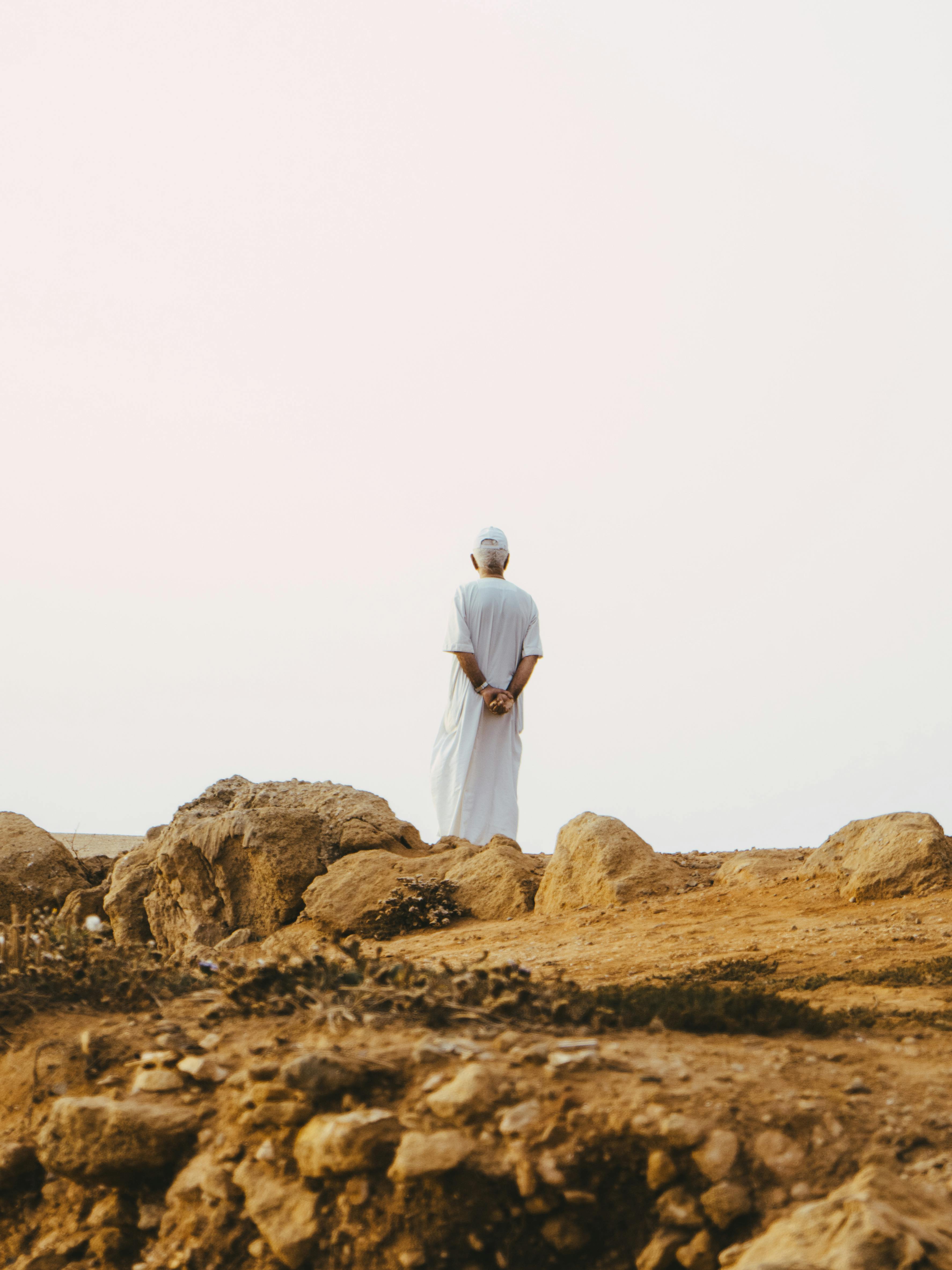 A solitary figure in traditional attire stands in a desert landscape in Rabat, Morocco, evoking solitude and contemplation.