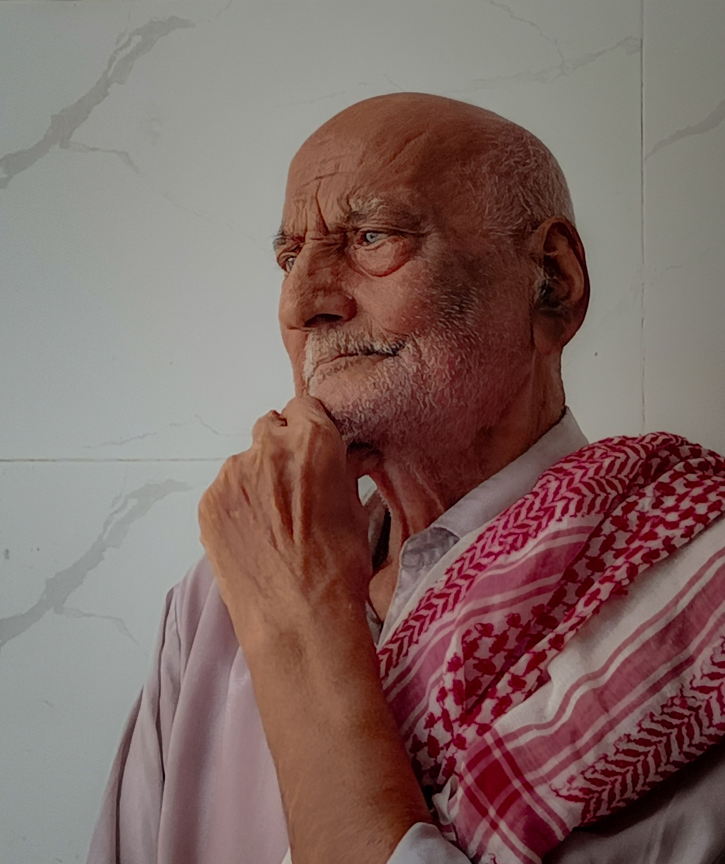 Portrait of an elderly man deep in thought, wearing a traditional checkered scarf.