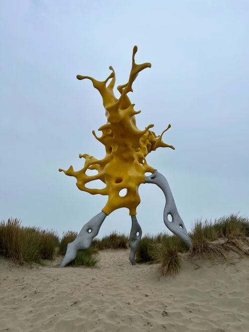 Free A vibrant yellow abstract sculpture on a coastal sand dune, creating a surreal beach landscape. Stock Photo