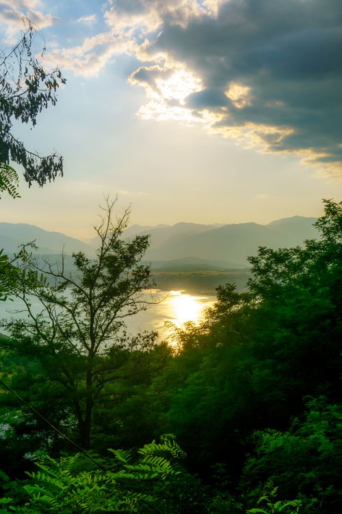 Free Beautiful sunset over a tranquil mountain lake with lush greenery and dramatic sky. Stock Photo