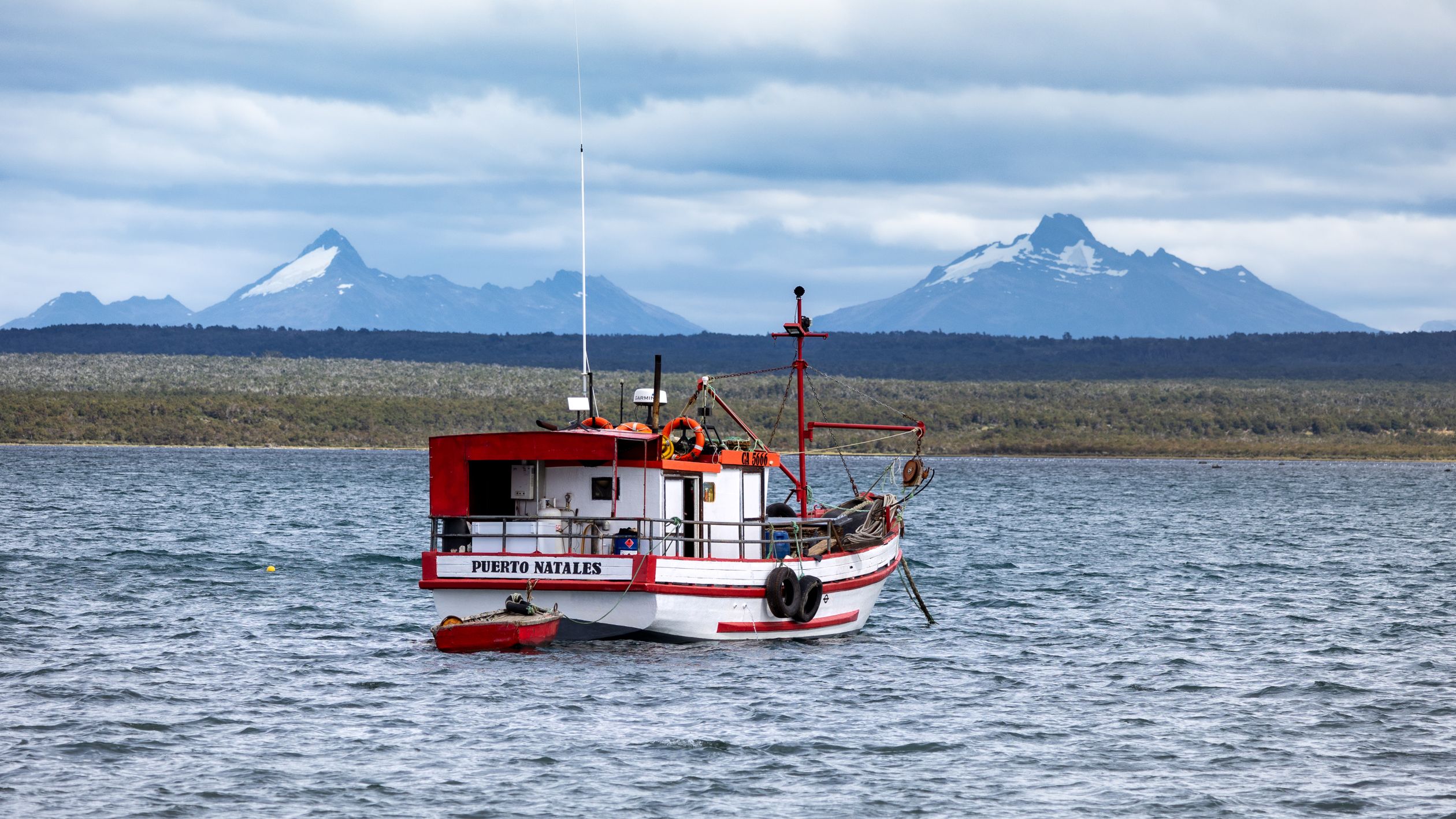 A wooden fishing boat floats on calm waters with mountains in the background, Puerto Natales.