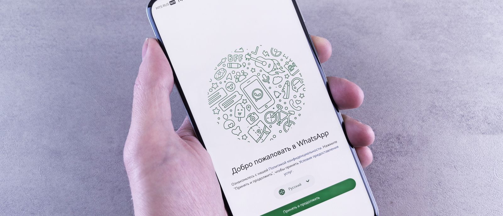 Tampilan dekat tangan yang memegang telepon pintar menampilkan layar selamat datang WhatsApp dalam bahasa Rusia.