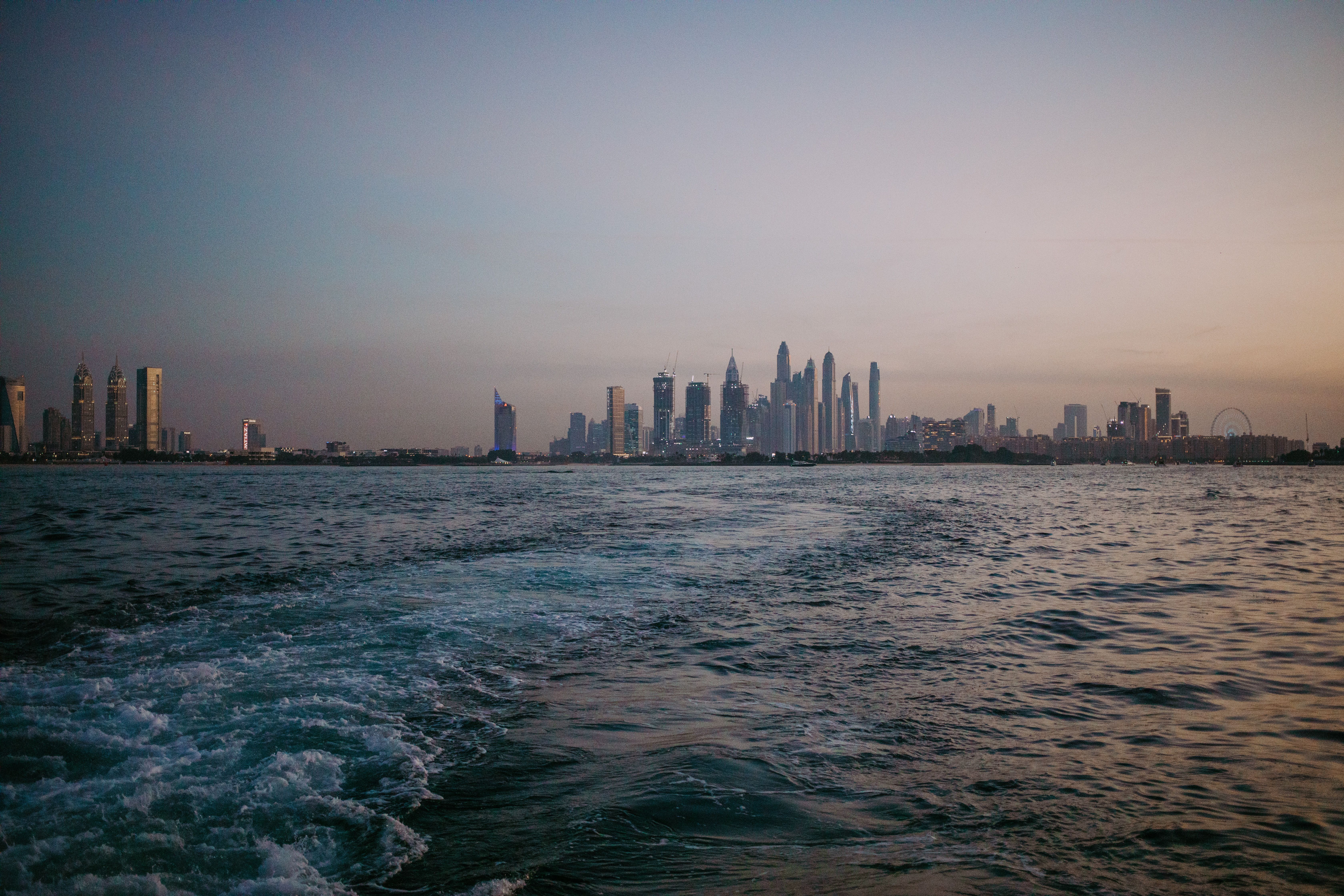 A breathtaking view of Dubai's skyline at dusk seen from the sea, reflected in calm waters.