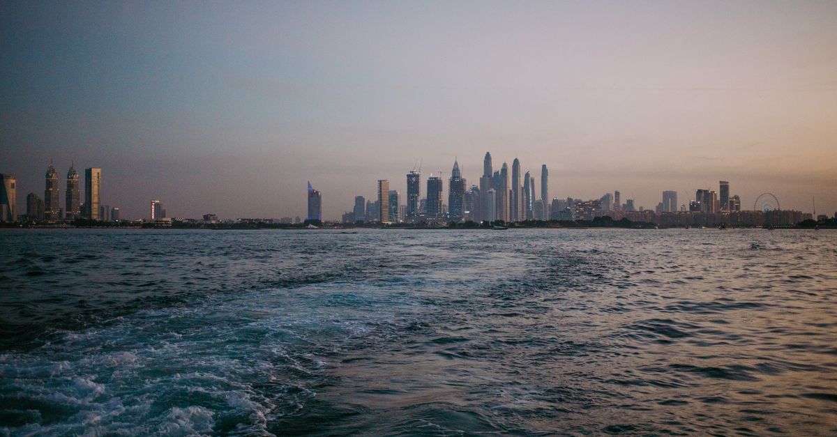 A breathtaking view of Dubai's skyline at dusk seen from the sea, reflected in calm waters.
