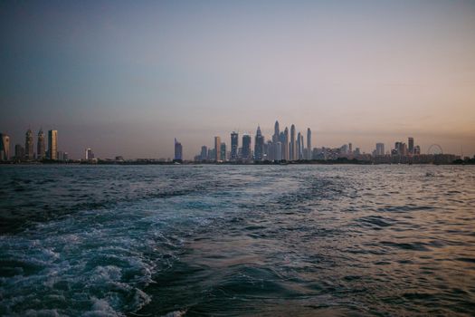 A breathtaking view of Dubai's skyline at dusk seen from the sea, reflected in calm waters.