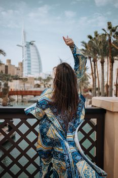 Back view of a woman in colorful attire enjoying the scenic view of Burj Al Arab in Dubai, UAE.