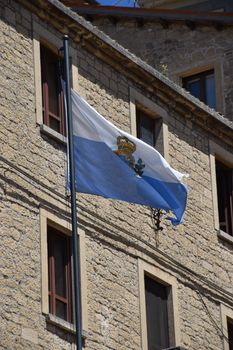 San Marino flag waving against a historic stone building under a clear blue sky.
