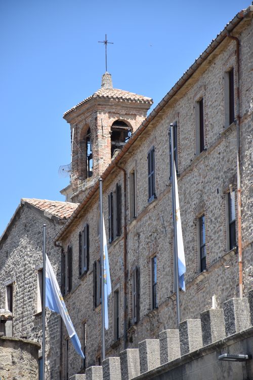 Free Rustic stone building with flags in San Marino against a clear blue sky. Stock Photo