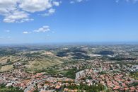 A panoramic aerial view of San Marino's rolling hills and cityscape under a clear blue sky.