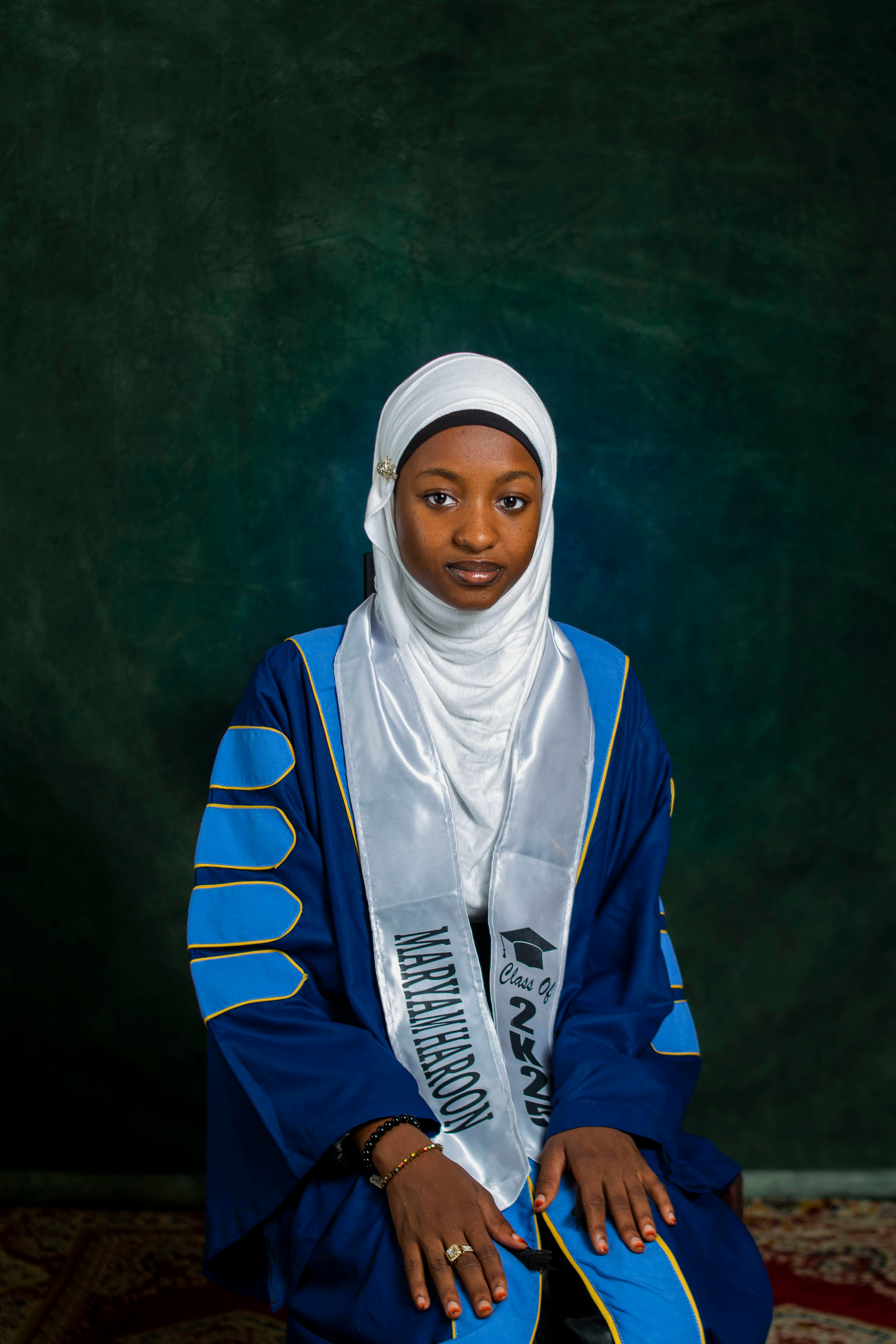 Young woman in hijab and graduation gown with proud expression.