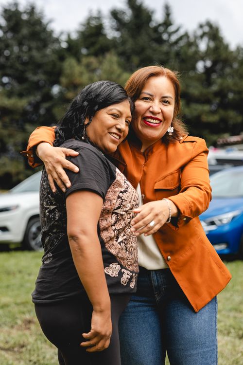 Free Two women sharing a joyful embrace outdoors with cars in the background, expressing friendship. Stock Photo