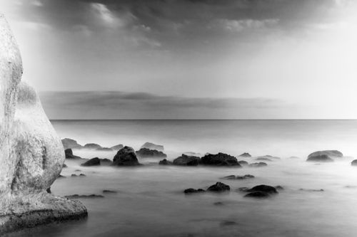 Free A serene black and white seascape featuring rocky shoreline under a dramatic sky. Stock Photo