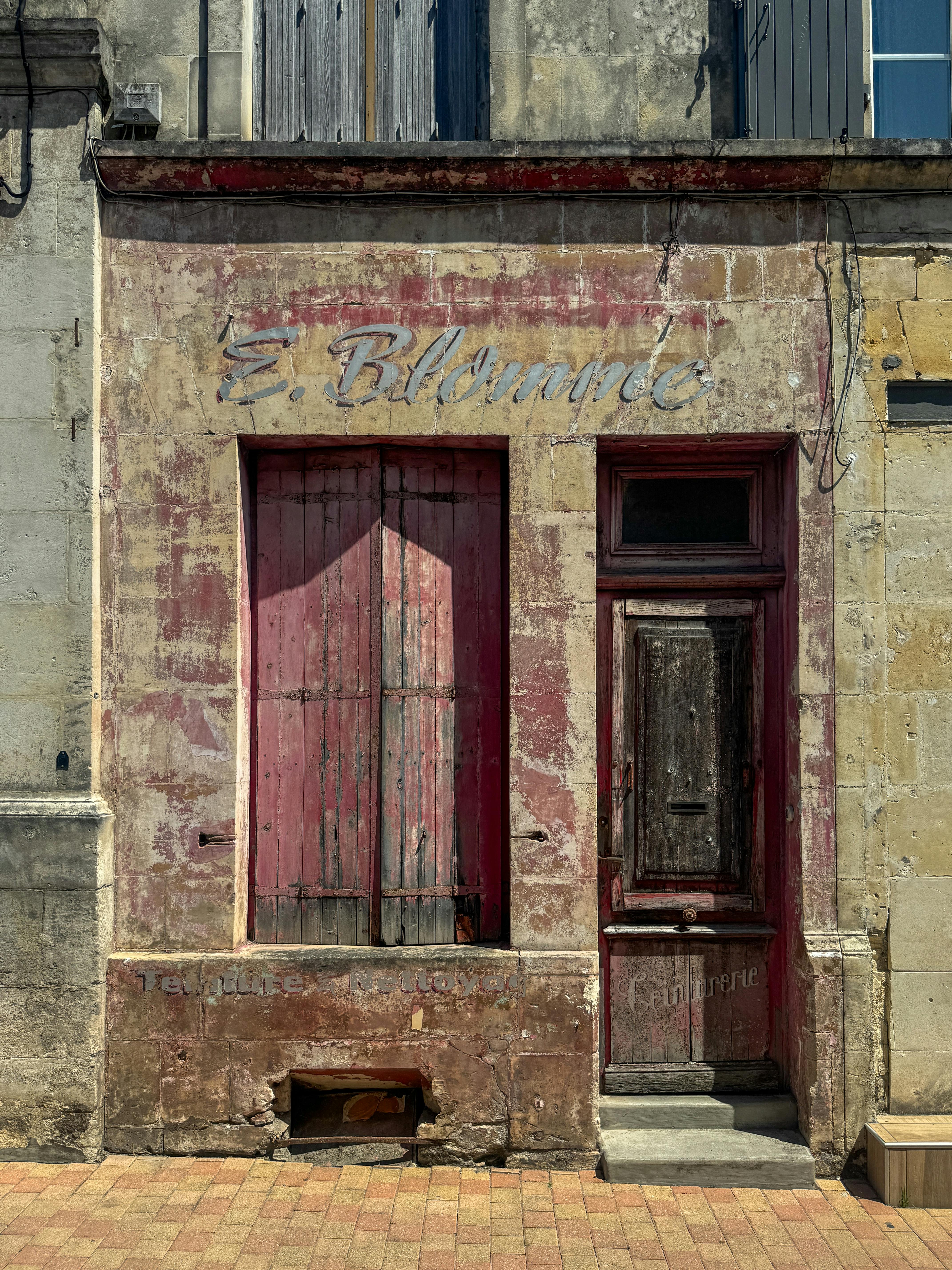 Vintage French shopfront with faded red doors and text, capturing the rustic charm of Jonzac.