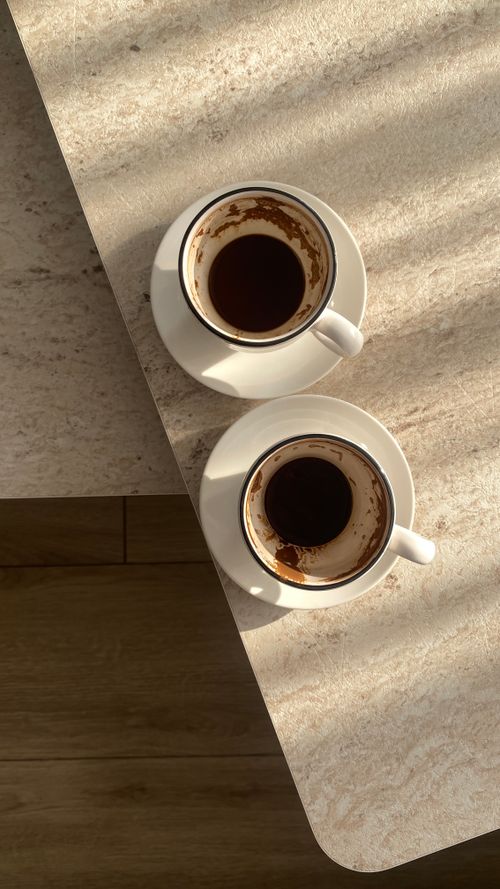 Free Two empty coffee cups casting shadows on a sunlit marble table, creating a warm and inviting scene. Stock Photo