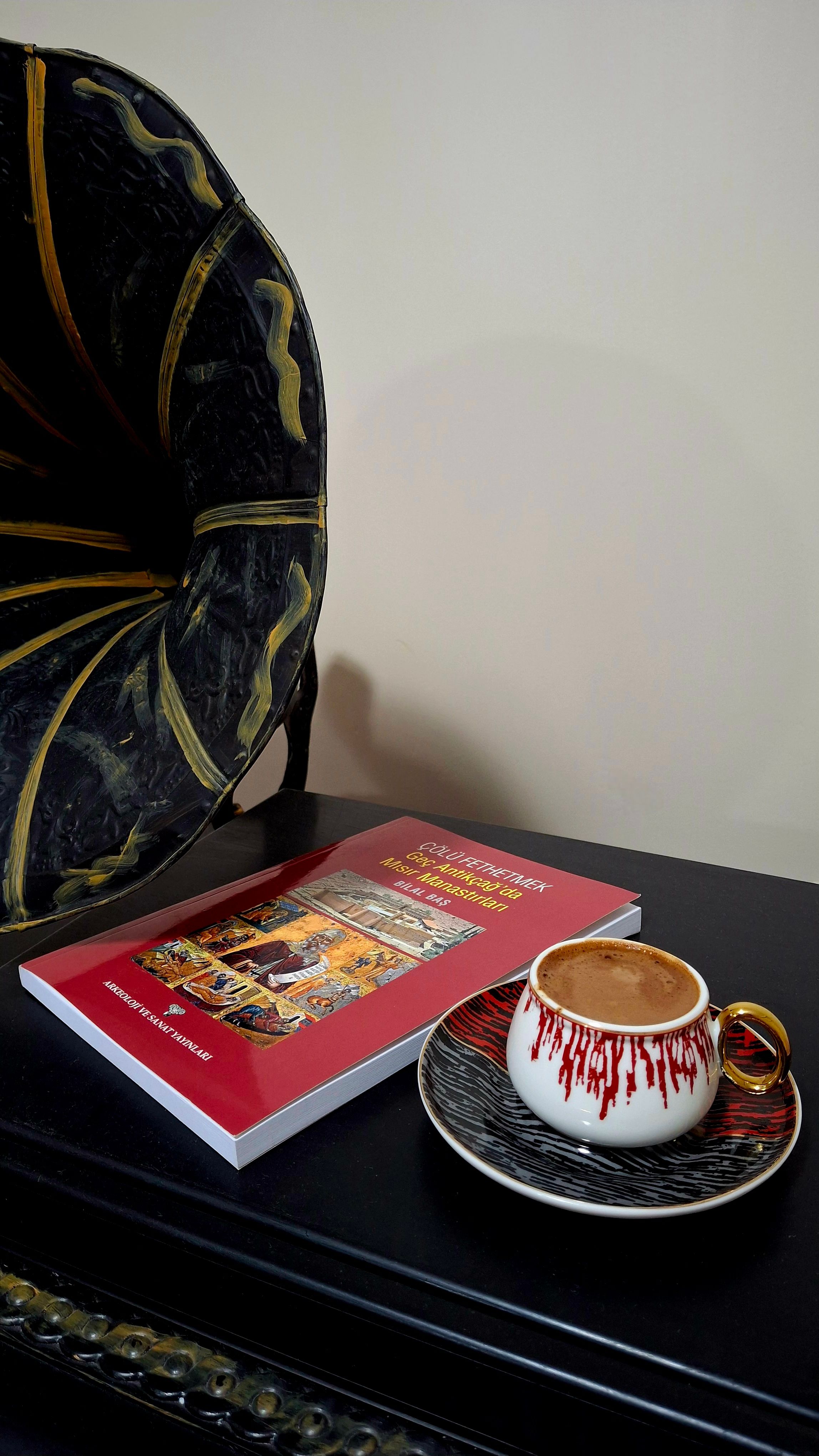 A close-up of a vintage phonograph, cup of coffee, and book on a table, indoors.