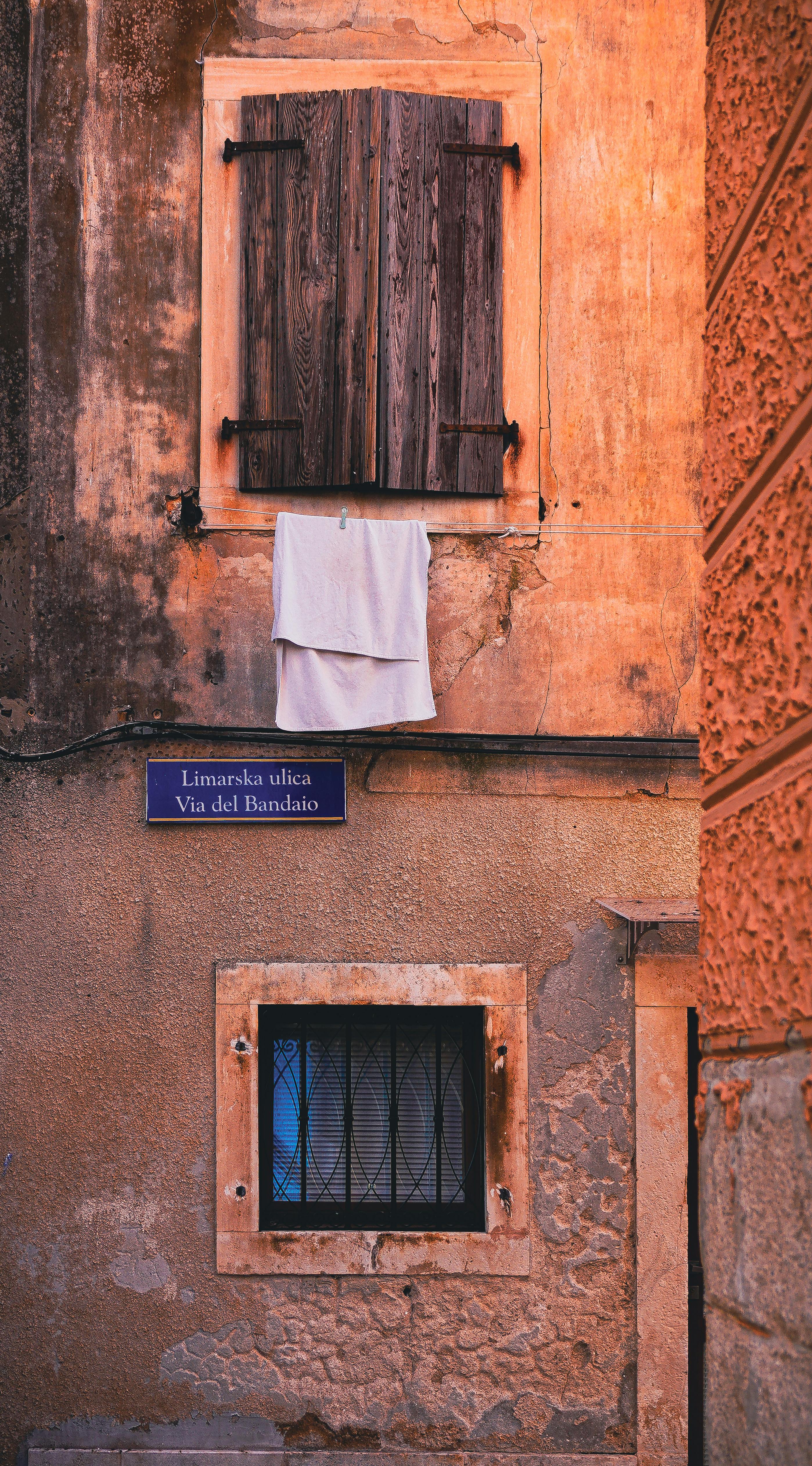 Rustic wall with wooden shutters and street sign in a quaint European alley.