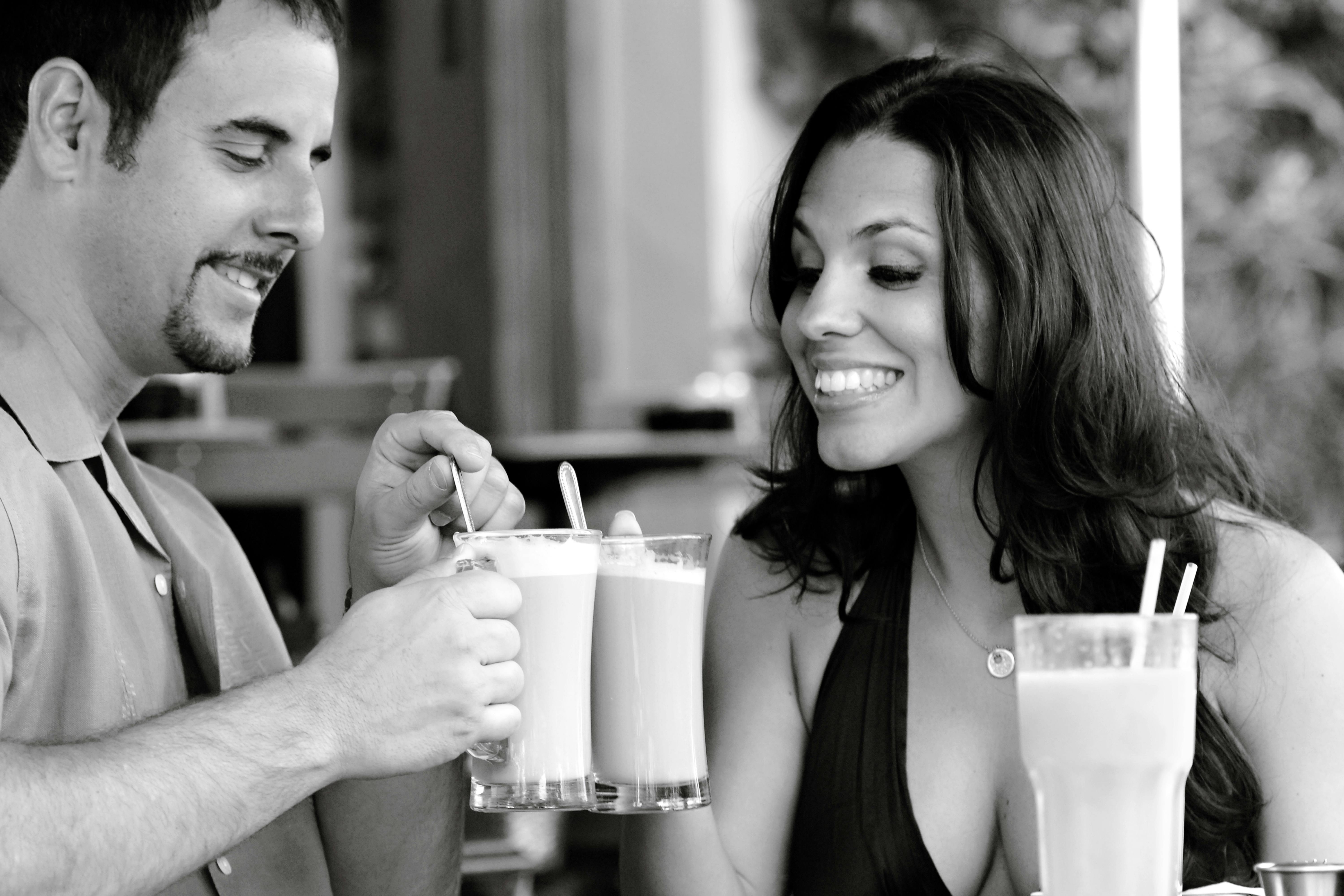 Smiling couple enjoying lattes at an outdoor Miami Beach cafe, sharing a joyful moment.