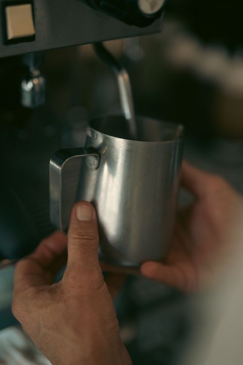 Free Close-up of a barista frothing milk in a metal jug with an espresso machine in a café. Stock Photo