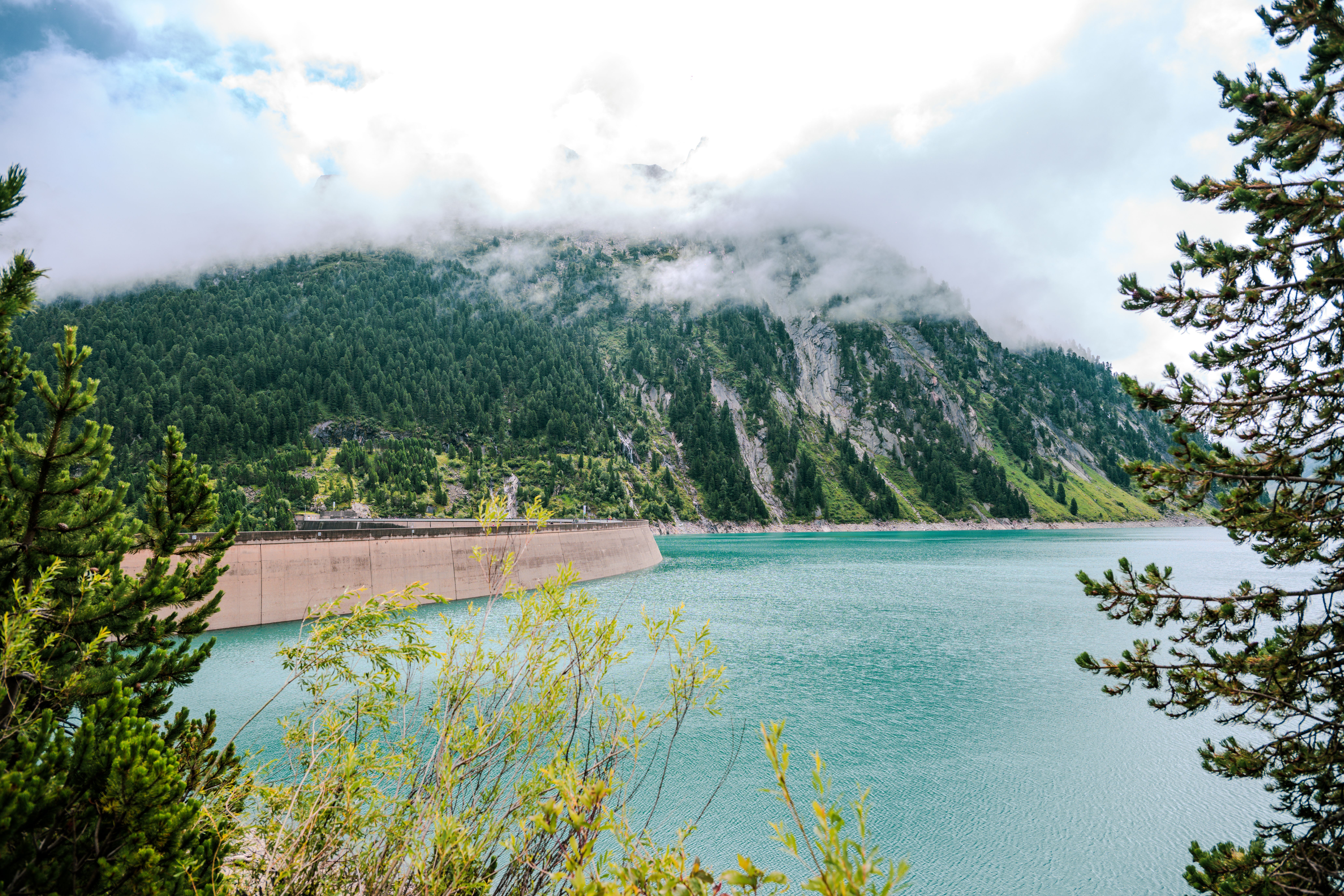 Serene alpine landscape with a turquoise lake and misty mountains in Tirol, Austria.
