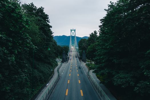 Capture of Lions Gate Bridge in Vancouver, British Columbia, bordered by lush greenery and mountains in the background.