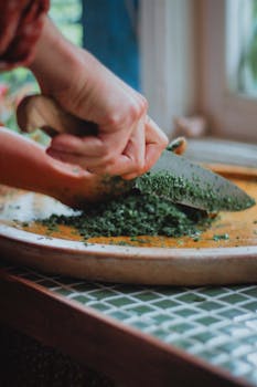 A close-up of hands skillfully chopping fresh herbs on a wooden cutting board in a kitchen.