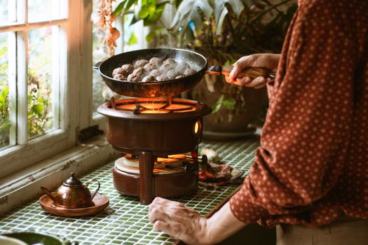Warm kitchen setting with meatballs cooking over a vintage stove, framed by green plants.