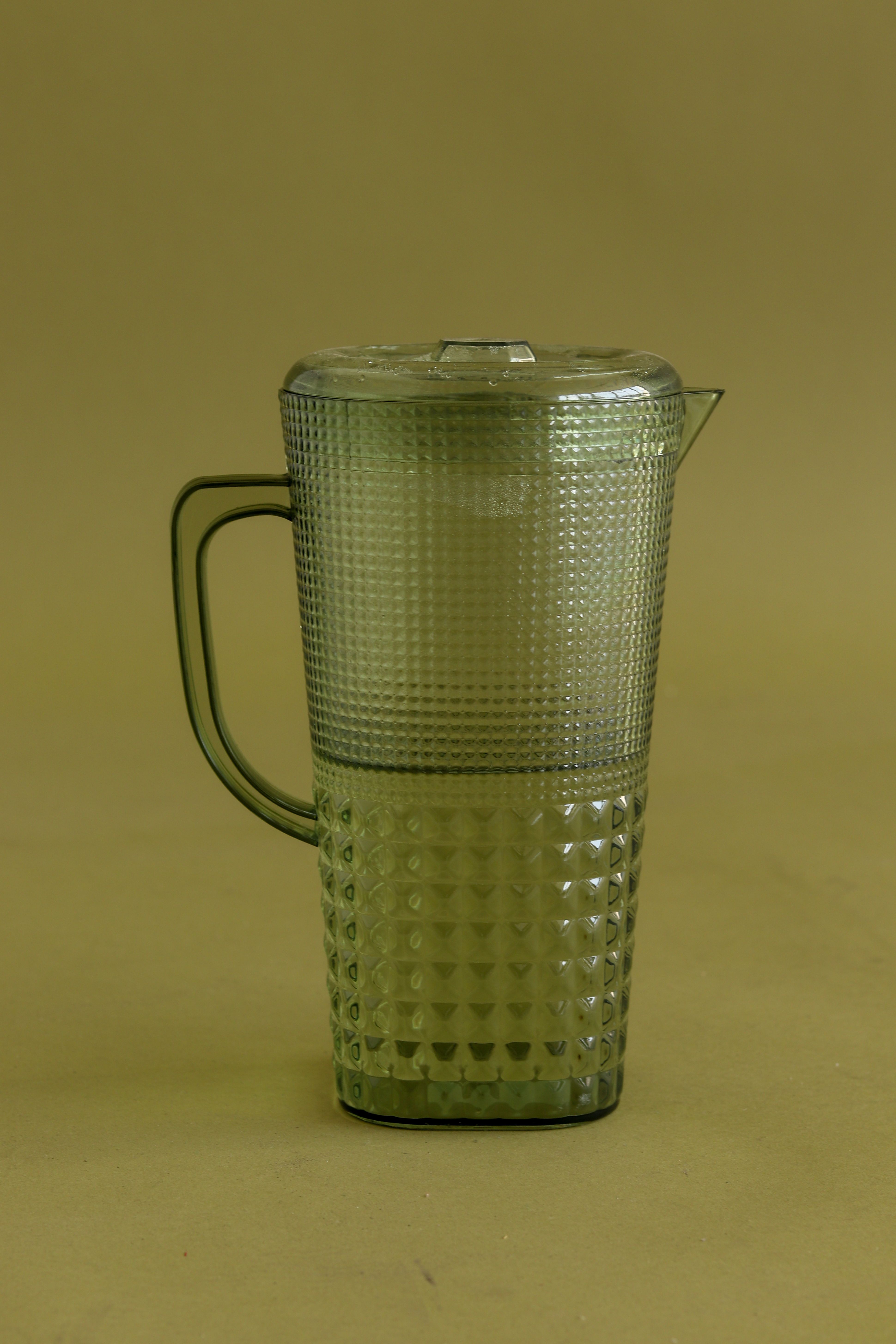 Fotomural Una jarra de agua clásica de vidrio verde vintage con un diseño texturizado intrincado sobre un fondo neutro.