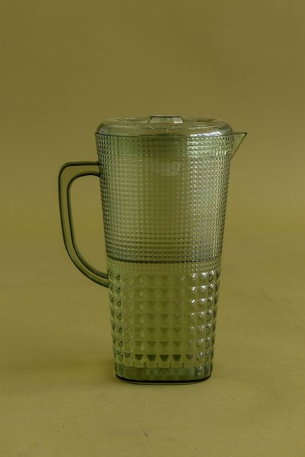 Fotomural Una jarra de agua clásica de vidrio verde vintage con un diseño texturizado intrincado sobre un fondo neutro.